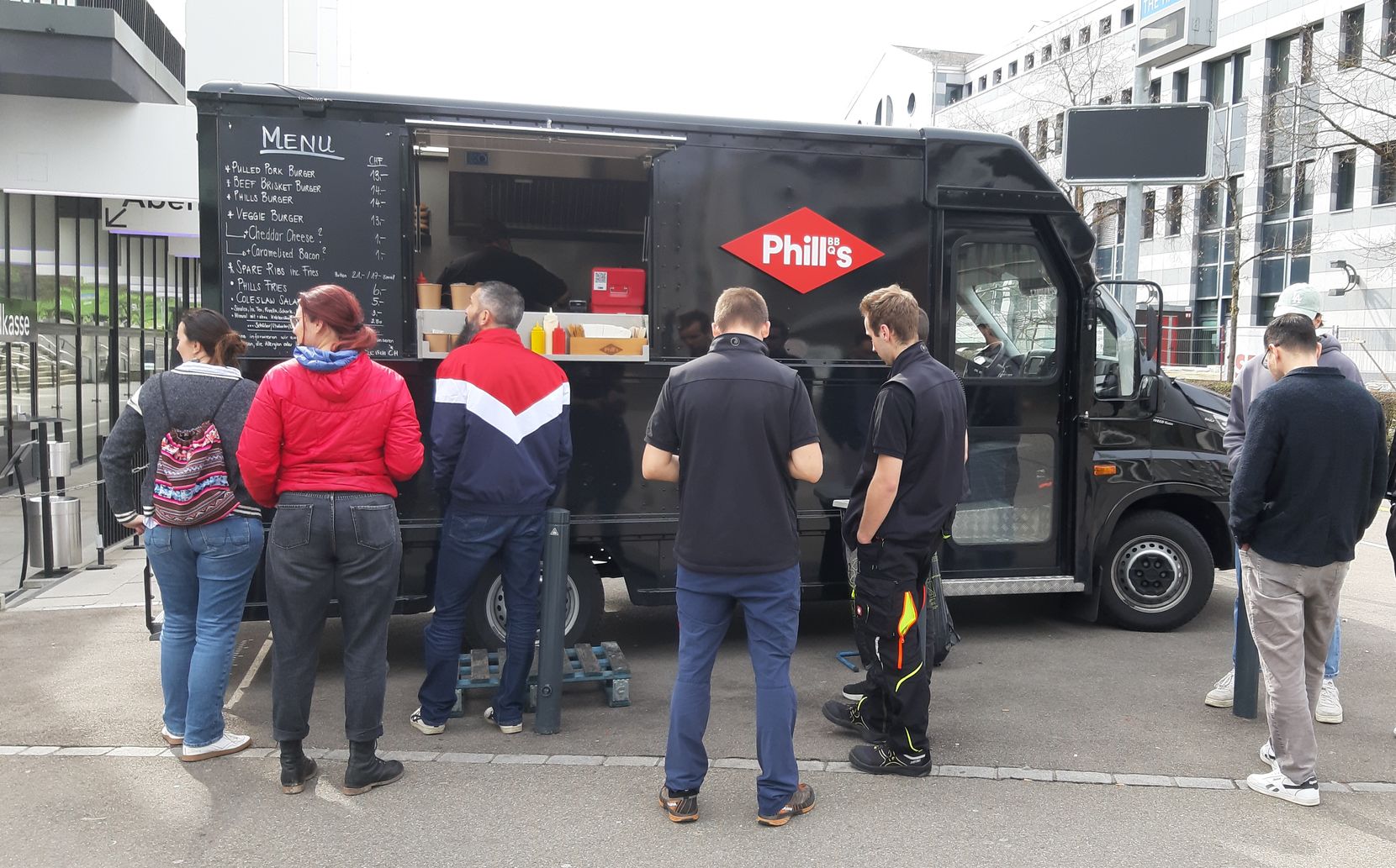 Menschen stehen vor einem schwarzen Foodtruck an. 